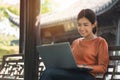 Happy young asian woman be smile working with her laptop on a bench in the park outdoors on vacation time Royalty Free Stock Photo