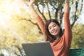 Happy young asian woman be smile working with her laptop and hand up on a bench in the park outdoors on vacation time Royalty Free Stock Photo