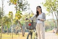 Happy young Asian woman walking on the sidewalk in the beautiful greenery park with her bicycle Royalty Free Stock Photo