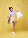 Happy young asian woman celebrating with mobile phone and holding shopping bags isolated over yellow background Royalty Free Stock Photo