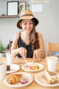 Happy young asian woman eating dessert with croissant, cake and iced coffee on wooden table