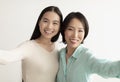 Happy young Asian woman and her mature mother taking selfie together on white studio background Royalty Free Stock Photo