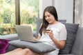 Happy young asian woman holding credit card and laptop sitting on sofa at home Royalty Free Stock Photo