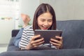 Happy young Asian woman holding a digital tablet and using online social lifestyle on sofa in the home. Royalty Free Stock Photo