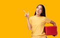 Happy young asian woman holding red gift pointing up to copy space Standing over yellow background Beautiful Girl happy smile hold Royalty Free Stock Photo