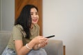 Happy young asian woman holding remote control, watching television on comfortable sofa at home Royalty Free Stock Photo