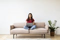 Happy young asian woman with laptop sitting cross-legged on sofa at home Royalty Free Stock Photo