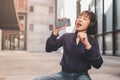 Happy young asian woman listening to music with headphones via smartphone and having fun while sitting side the street. Royalty Free Stock Photo