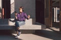 Happy young asian woman listening to music with headphones via smartphone and having fun while sitting side the street. Royalty Free Stock Photo