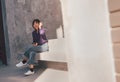 Happy young asian woman listening to music with headphones via smartphone and having fun while sitting side the street. Royalty Free Stock Photo