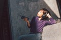 Happy young asian woman listening to music with headphones via smartphone and having fun while sitting side the street. Royalty Free Stock Photo