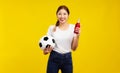 Happy Young Asian woman over isolated yellow background holding a soccer ball and drinks Royalty Free Stock Photo