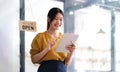 Happy young Asian woman owner standing holding a tablet with open sign board. Royalty Free Stock Photo