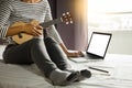 Happy young asian woman playing ukulele sitting on bed in bedroom. Royalty Free Stock Photo