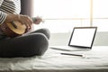 Happy young asian woman playing ukulele sitting on bed in bedroom. Royalty Free Stock Photo