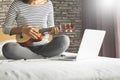 Happy young asian woman playing ukulele sitting on bed in bedroom. Royalty Free Stock Photo