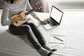 Happy young asian woman playing ukulele sitting on bed in bedroom. Royalty Free Stock Photo