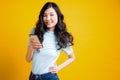 Happy young Asian woman posing with smartphone in front of the yellow background.