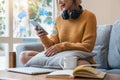 Happy young asian woman relax on comfortable couch at home smiling girl use cellphone browse wireless internet on Royalty Free Stock Photo