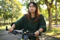 Happy young Asian woman riding a bicycle through the city park. Active urban lifestyle concept.