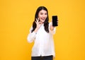 Happy young Asian woman showing at blank screen mobile phone and hand gesture ok isolated over yellow background Royalty Free Stock Photo
