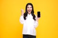 Happy young Asian woman showing at blank screen mobile phone and hand gesture success isolated over yellow background Royalty Free Stock Photo