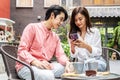 Happy Young asian woman sitting with boyfriend at cafe table, discussing over on smartphone, Young couple looking at mobile phone Royalty Free Stock Photo