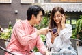 Happy Young asian woman sitting with boyfriend at cafe table, discussing over on smartphone, Young couple looking at mobile phone Royalty Free Stock Photo