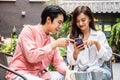 Happy Young asian woman sitting with boyfriend at cafe table, discussing over on smartphone, Young couple looking at mobile phone Royalty Free Stock Photo