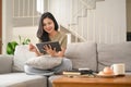 Happy young asian woman sitting in bright living room and using digital tablet on couch Royalty Free Stock Photo