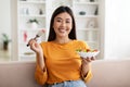 Happy young asian woman sitting on couch, eating salad Royalty Free Stock Photo