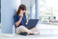 Happy young Asian woman sitting and talking on her phone while using her laptop computer outside of her office building Royalty Free Stock Photo