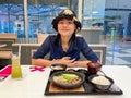 Happy young Asian woman smiling and enjoying eating Japanese food in a restaurant during coronavirus or covid-19 outbreak Royalty Free Stock Photo