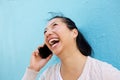 Happy young asian woman talking on mobile phone against blue wall Royalty Free Stock Photo