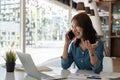 Happy young asian woman talking on the mobile phone and smiling while sitting at her working with laptop and paperwork Royalty Free Stock Photo