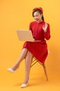 Happy young Asian woman using laptop in armchair over orange background Royalty Free Stock Photo