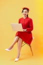 Happy young Asian woman using laptop on chair over orange background Royalty Free Stock Photo