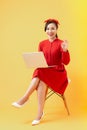 Happy young Asian woman using laptop on chair over orange background Royalty Free Stock Photo