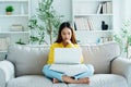 Happy young Asian woman using laptop while seated on couch Royalty Free Stock Photo