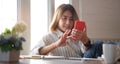 Happy young Asian woman using mobile phone while sitting at her workspace Royalty Free Stock Photo