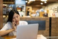Happy young Asian woman using phone and working with a laptop in the coffee shop cafe office. Royalty Free Stock Photo