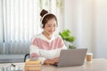 A happy young Asian woman wearing eyeglasses and headphones is using her laptop at a table Royalty Free Stock Photo