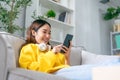 Happy young asian woman wearing headset and relaxing on comfortable couch at home