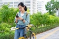 Happy young Asian woman in work clothes using smartphone with bicycle in outdoor park. Eco-friendly concept Royalty Free Stock Photo