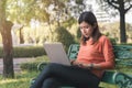 Happy young asian woman working with her laptop on a bench in the park outdoors on vacation time Royalty Free Stock Photo