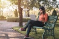 Happy young asian woman working with her laptop on a bench in the park outdoors on vacation time Royalty Free Stock Photo