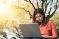 Happy young asian woman  working with her laptop on a bench in the park outdoors on vacation time Royalty Free Stock Photo