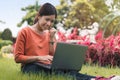 Happy young asian woman working with her laptop on a bench in the park outdoors on vacation time Royalty Free Stock Photo