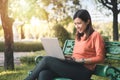 Happy young asian woman working with her laptop on a bench in the park outdoors on vacation time Royalty Free Stock Photo