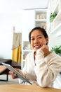 Happy young Asian woman working at home office holding tablet looking at camera. Royalty Free Stock Photo